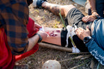 Person using a compact vehicle first aid kit to treat an injured leg in an outdoor setting.