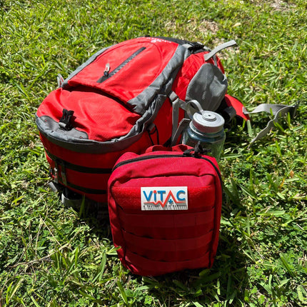 ViTAC Adventurer First Aid Kit with red backpack and water bottle on grass, ideal for outdoor activities.