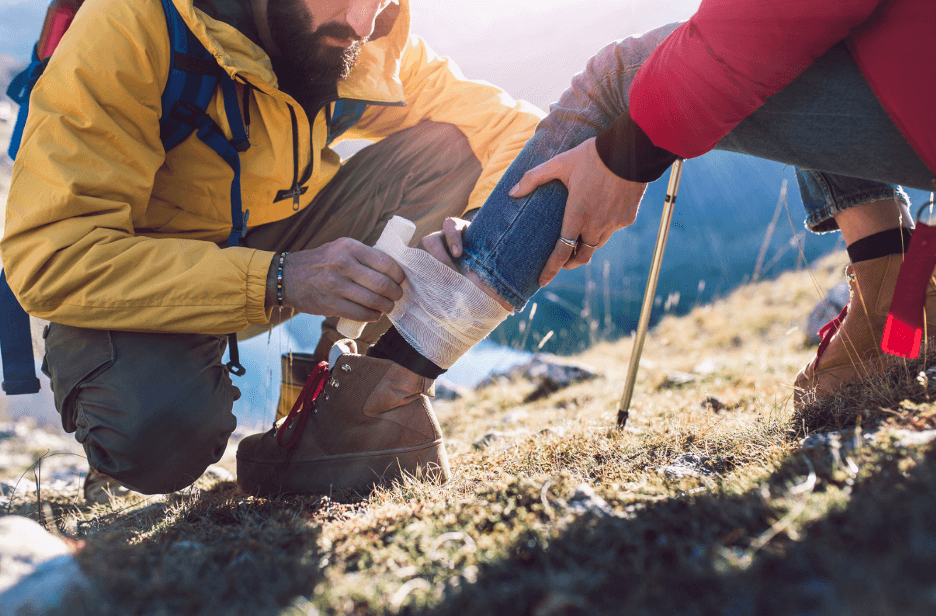 Individual applying conforming gauze vs. elastic bandages to injured leg outdoors.