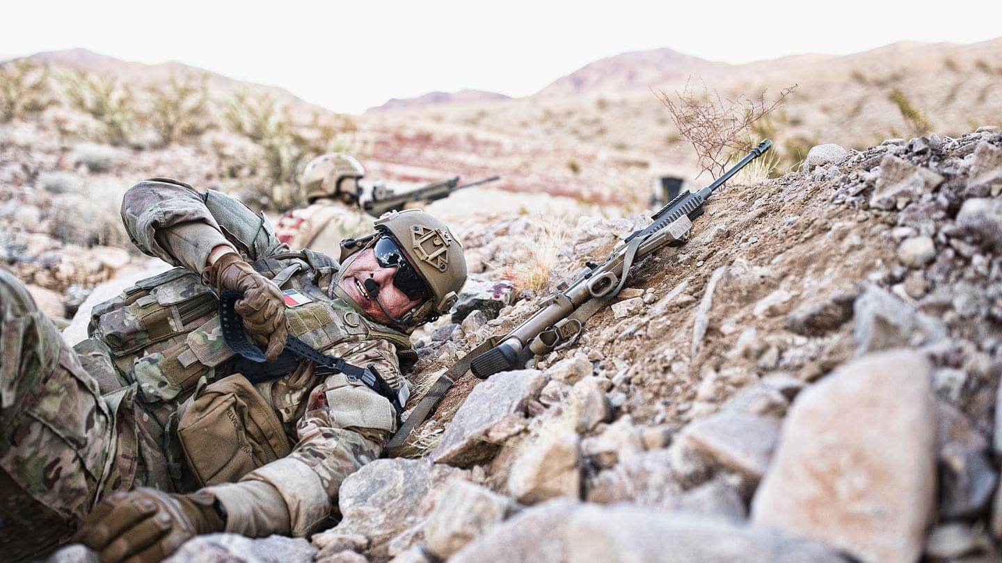 First Aid Kit vs. Trauma Kit: Why You Need Both - soldier in tactical gear taking cover in rocky terrain.