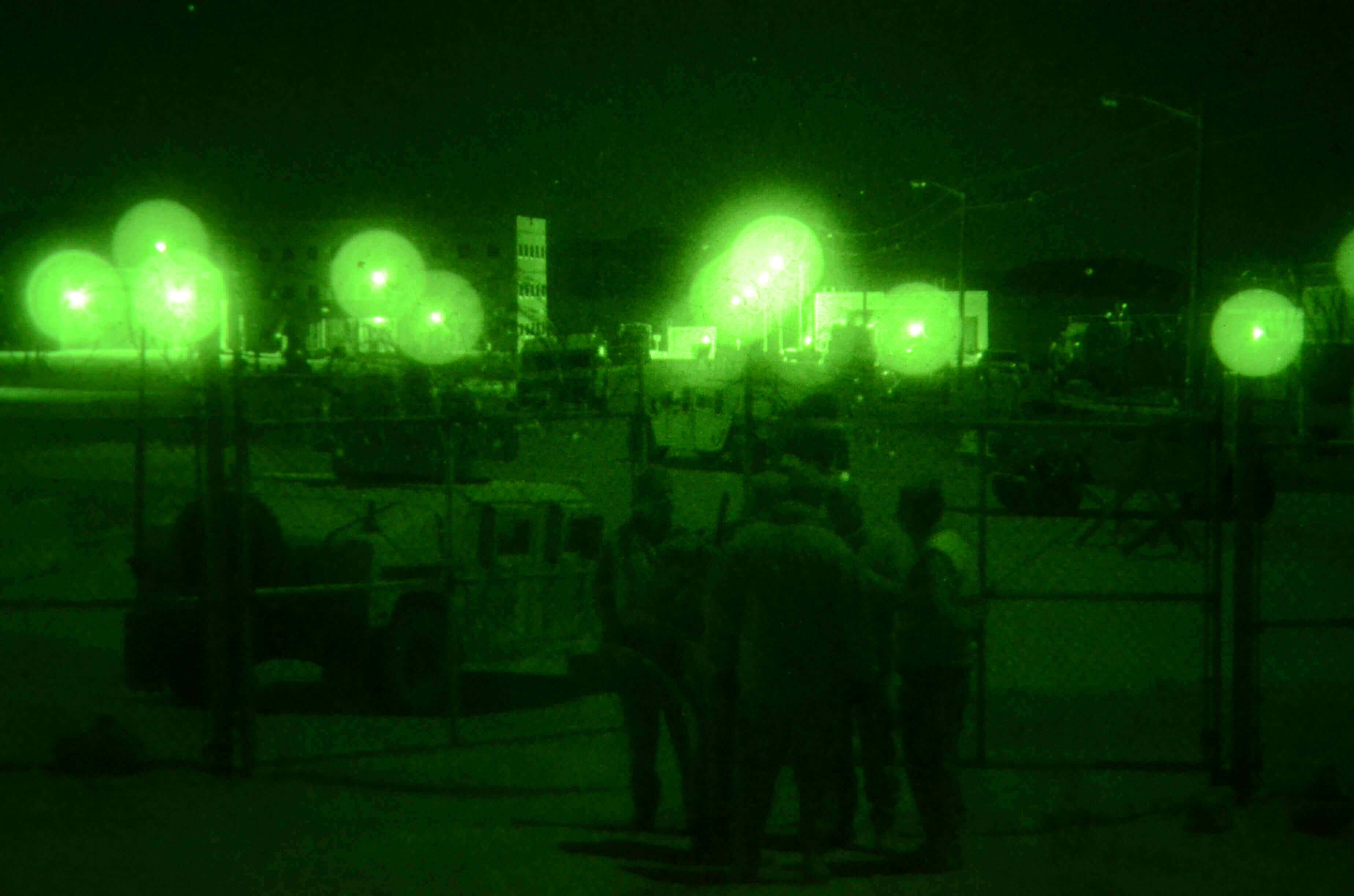 What is a Green Beret training under night vision with soldiers and equipment in the background.