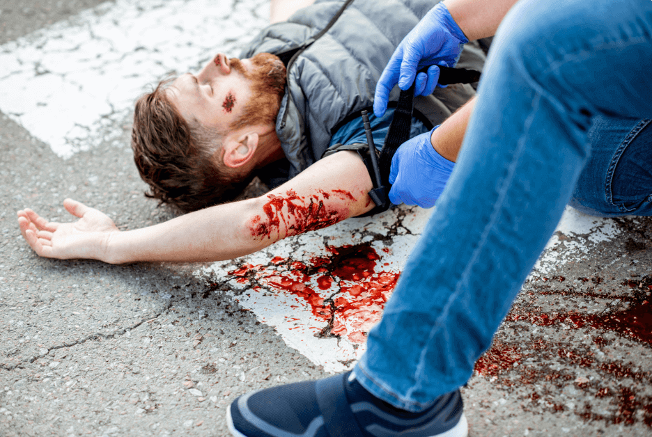 A person applying a tourniquet to a severely injured arm at the scene of an accident.