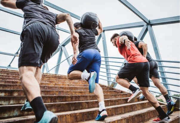 Athletes engaging in tactical preparedness training while running up stairs with medicine balls for emergency readiness.