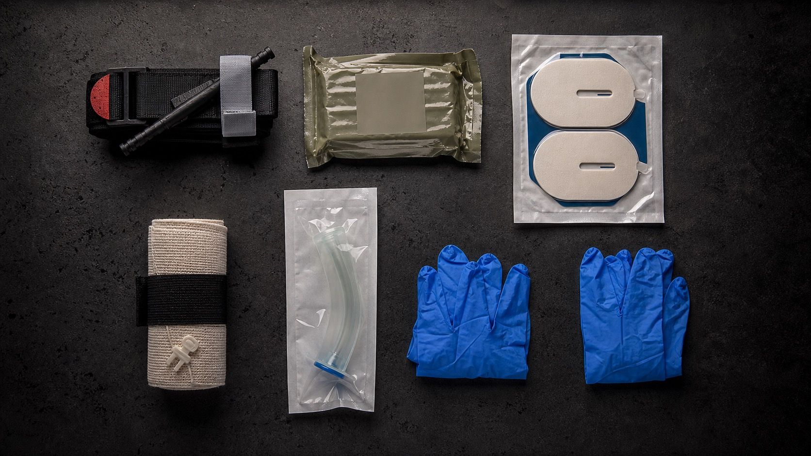 TCCC gunshot wound kit components flat lay on dark surface