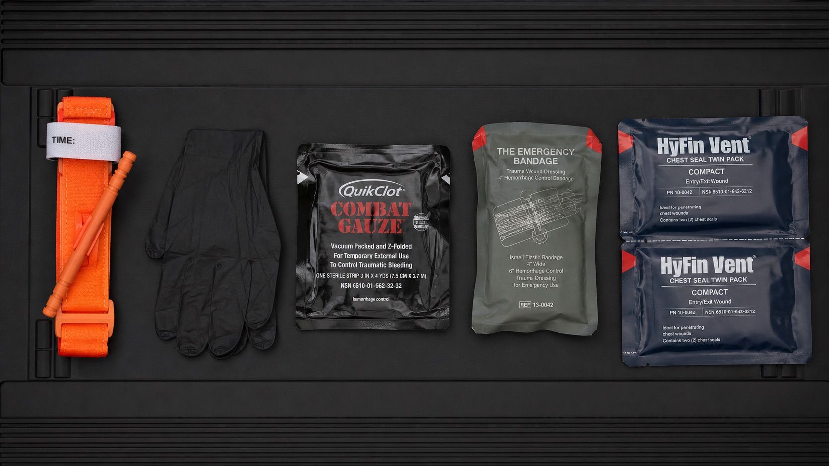 Five essential trauma kit items laid out on tactical surface