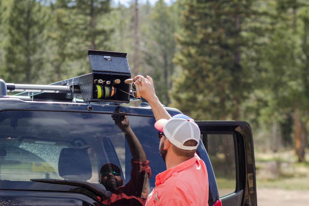 Person preparing fishing gear from a vehicle trauma kit essentials setup on the roof of a car outdoors.