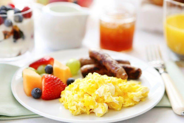 Plate of delicious breakfast featuring scrambled eggs, sausage, and mixed fruit including strawberries and blueberries.