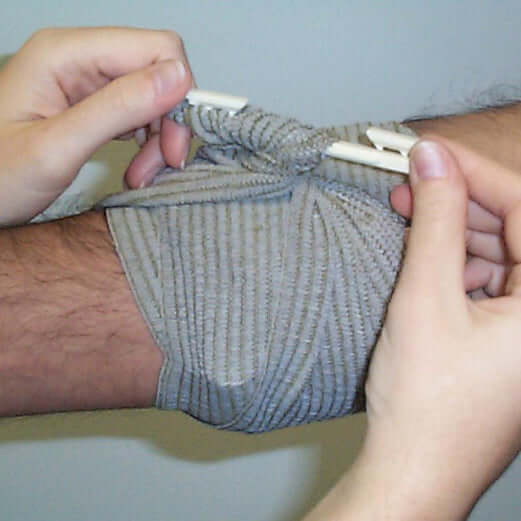 Applying a 4" Israeli Bandage on an injured arm for effective hemorrhage control.