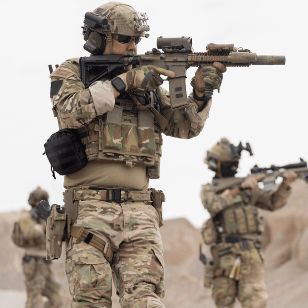 Soldiers in tactical gear practicing combat readiness in a rugged desert environment.