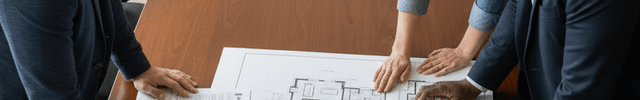 Three professionals discussing a building blueprint at a conference table in a modern office setting.