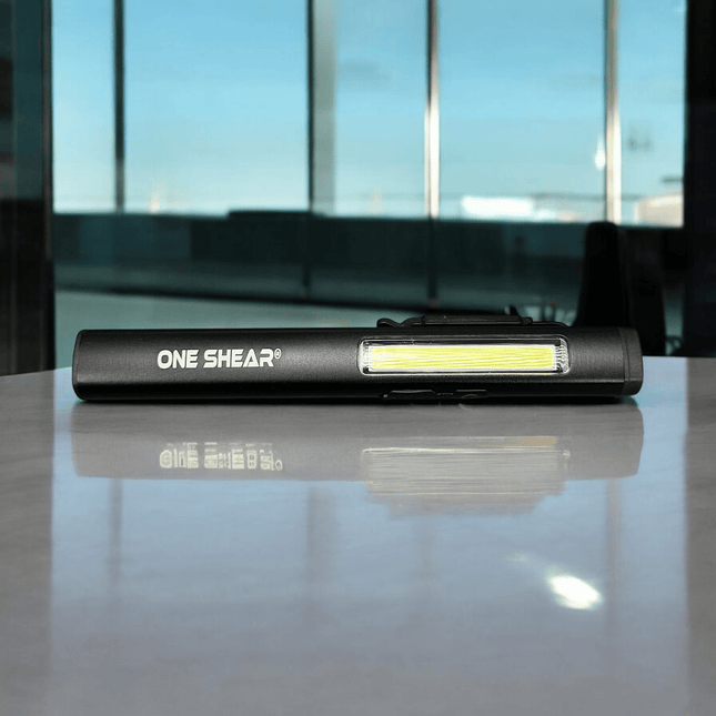 ONE SHEAR XPE+COB Magnetic Penlight shown on a reflective surface with a bright LED light.