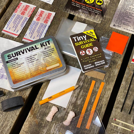 P-49 Elite Survival Kit - Bundle with essential survival items and Tiny Survival Guide laid out on a wooden surface.