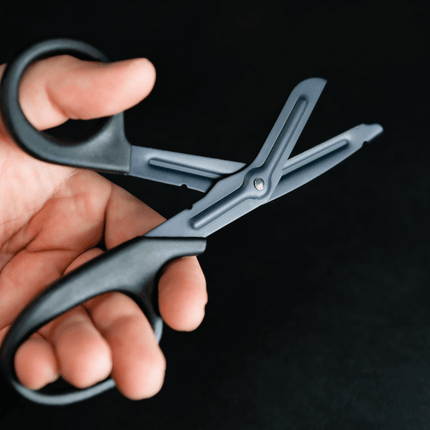 Lightweight medical scissors for EMT held in hand against a dark background, showcasing durable design and safety features.