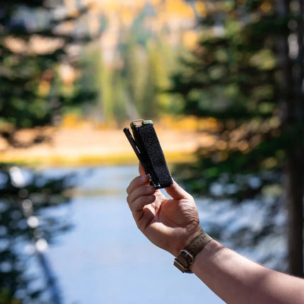 Hand holding Snakestaff Systems ETQ™ Gen 2 tourniquet against a scenic outdoor background.