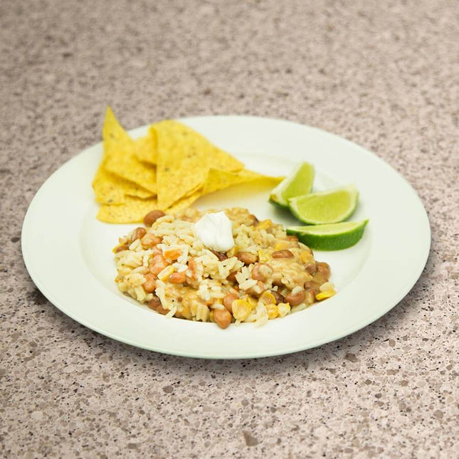 Plate of rice and beans topped with sour cream, served with tortilla chips and lime wedges.