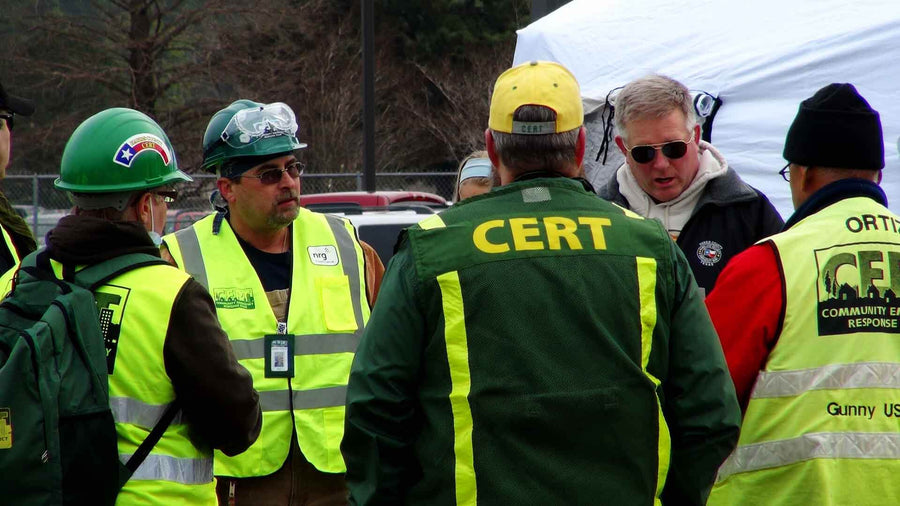 Group of CERT members in safety vests discussing emergency response strategy outdoors.