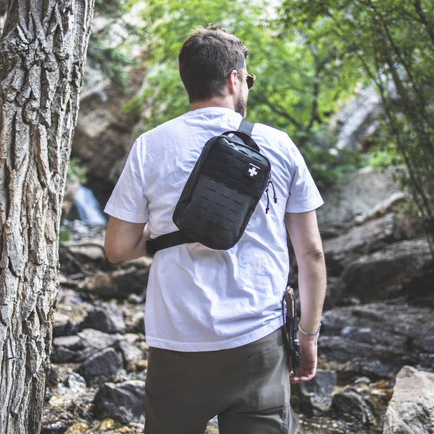 A man wearing the MyFAK First Aid Kit on his back in an outdoor setting near a rocky stream.