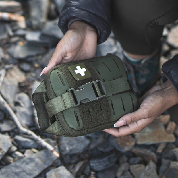 Person holding the Sidekick IFAK Pouch by MyMedic in a natural setting on rocky ground.