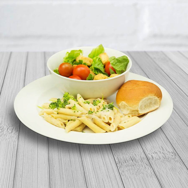 Plate of creamy pasta, mixed salad with cherry tomatoes, and a dinner roll on a wooden table.