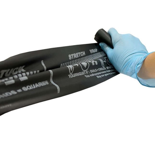 Close-up of a hand applying the SWAT T multipurpose latex-free tourniquet, demonstrating stretch and wrap technique.